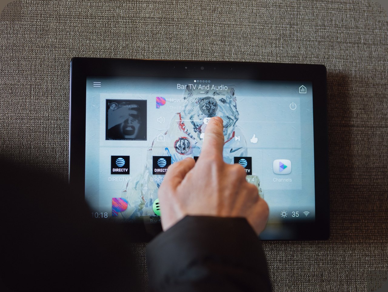 A hand tapping a wall-mounted touch panel to control the home's systems